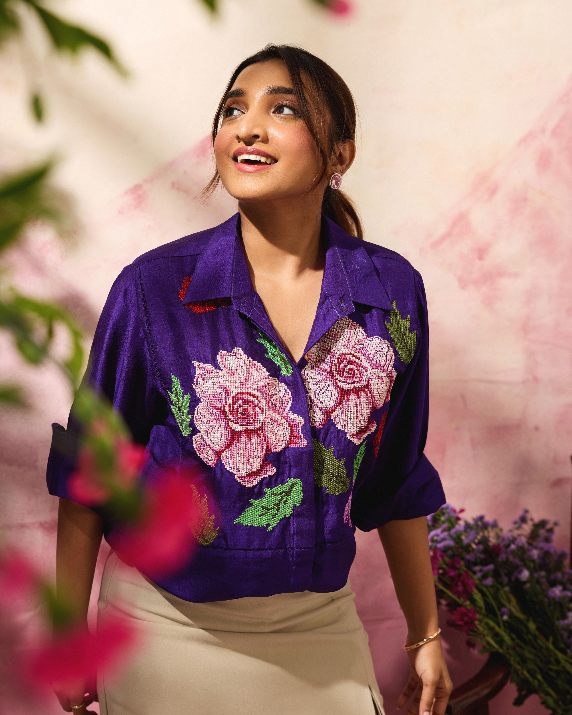 Woman wearing a purple embroidered shirt with floral designs against a pink floral background